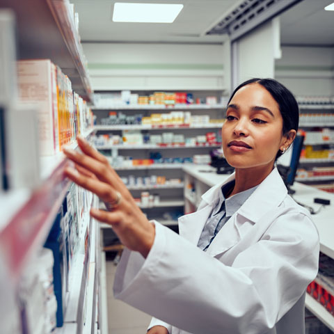 Young woman working in pharmacy looking for medicine in shelf standing behind counter Young woman working in pharmacy looking for medicine standing behind counter